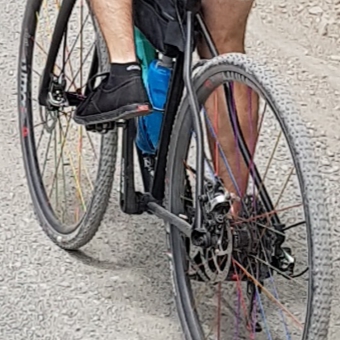 A slightly grainy, cropped close-up showing a cyclist pushing on pedals wearing black canvas shoes.