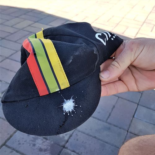 A black cycling cap with three stripes down the centre shows a small splatter of bird poop on the brim.