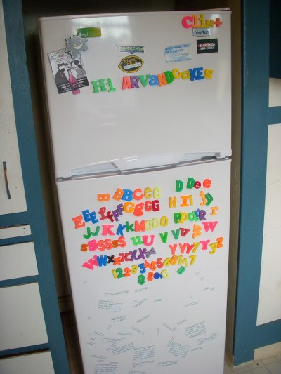 A refrigerator with a mess of multi-coloured alphabet fridge magnets, and magnetic poetry stuck to it.