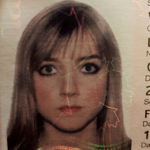 A passport photo of a young Laura (circa 2008). She has long dirty blonde hair which is cropped out of the photo, and bangs. She looks straight ahead at the camera, expressionless. She is wearing heavy black eye make up and excessive blush.