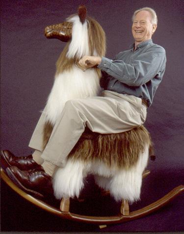 A random old white man with a big grin sits on a large rocking llama.