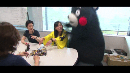 Animated gif of a rosy cheecked black bear mascot called Kumamon grabbing and tossing a woman dressed in a yellow kimono from her chair to the floor.