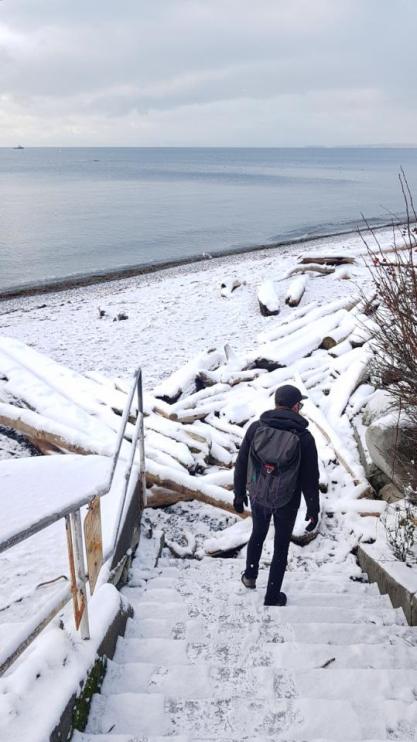 Yann, with his back turned to the camera, descends snowy steps leading to a snow-covered beach.