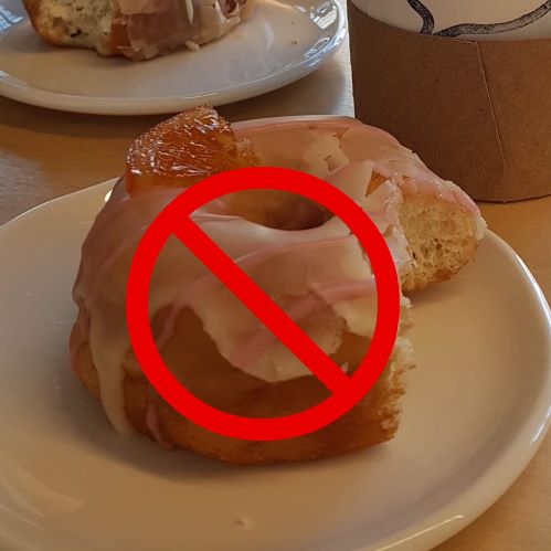A donut with a single bite taken out of it rests on a white plate. The circle with a slash symbol is shown overlapping the photo.