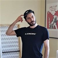 Yann, in a black cap and t-shirt which has the word LOOK printed across the chest, looks in the distance while scratching his head.