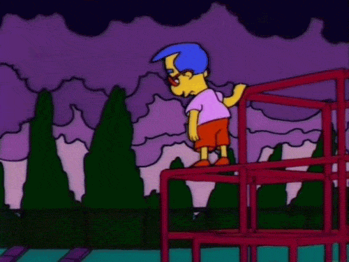 Gif of Milhouse standing on top of monkey bars while the wind whips his hair and the poplar trees in the background. Dark clouds are seen moving overhead.