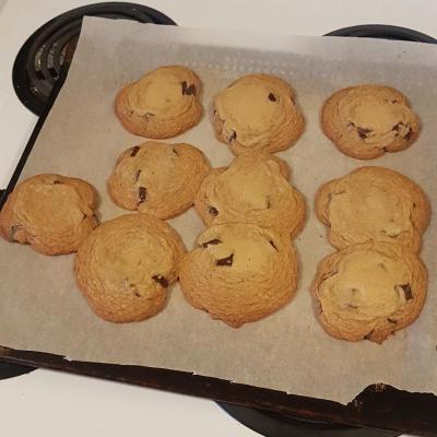 Ten chocolate chip cookies on a baking sheet that have mostly melted so that they're touching each other.