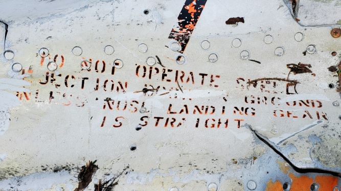 A crumpled metal panel reads DO NOT OPERATE SHELL EJECTION (word is illegible)  GROUND UNLESS NOSE LANDING GEAR IS STRAIGHT.