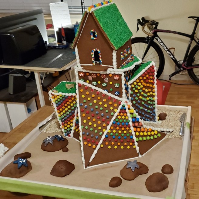 The front of a partially decorated gingerbread structure shows mounds of gingerbread arranged to resemble boulders. On three of the boulders are anthropomorphic starfish.