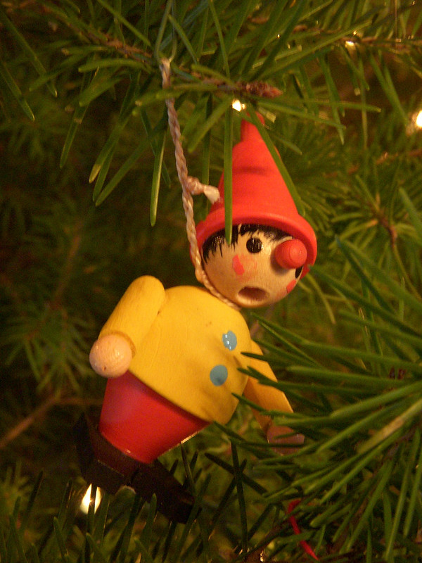 A wooden elf ornament with a hole for its mouth. It hangs from a branch by its neck.