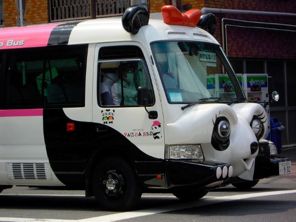The front of a bus modelled to look like a winking cartoon panda. The panda has a red bow between its ears.