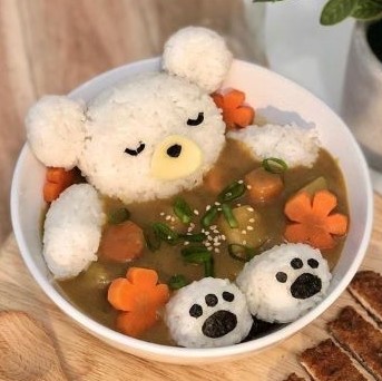 Rice balled together and arranged inside a bowl to resemble a sleeping bear relaxing in a bowl of broth. The carrots have been cut to resemble cherry blossoms.